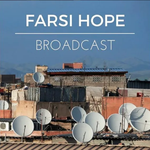 Rooftops with numerous satellite dishes against a blue sky and mountain background.