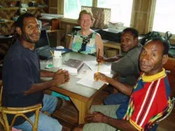 Four people sitting around a table, smiling, with papers and pencils in hand.