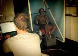 Man seated in a booth doing a breathing test while another person types on a laptop.