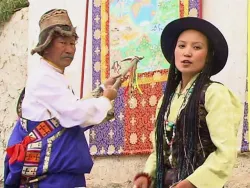 Un homme et une femme en costumes traditionnels colorés devant une tenture décorative.